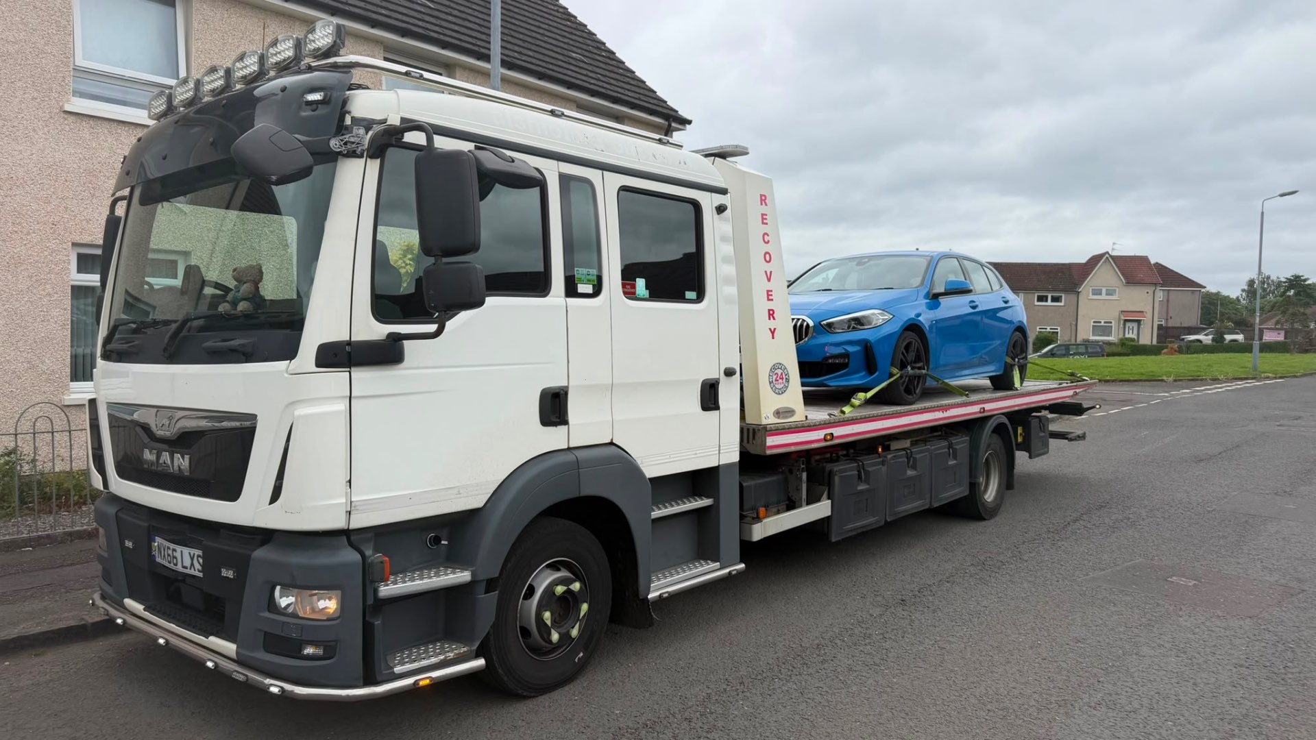 MAN 24-hour recovery truck with blue BMW 1 Series M Sport on flatbed outside house