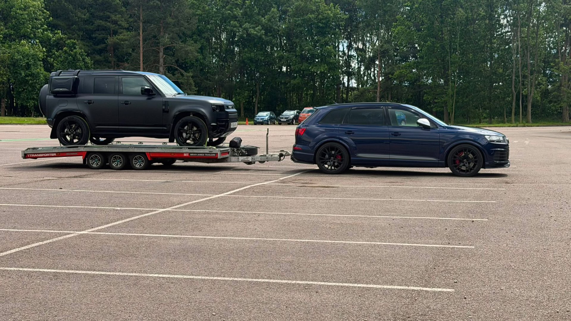 Matte black Land Rover Defender on covered transporter towed by Audi SQ7