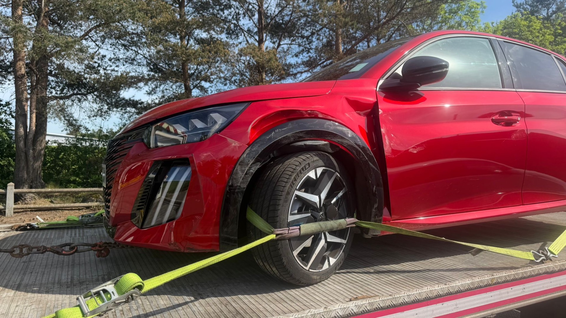Accident-damaged red Peugeot 208 on recovery flatbed
