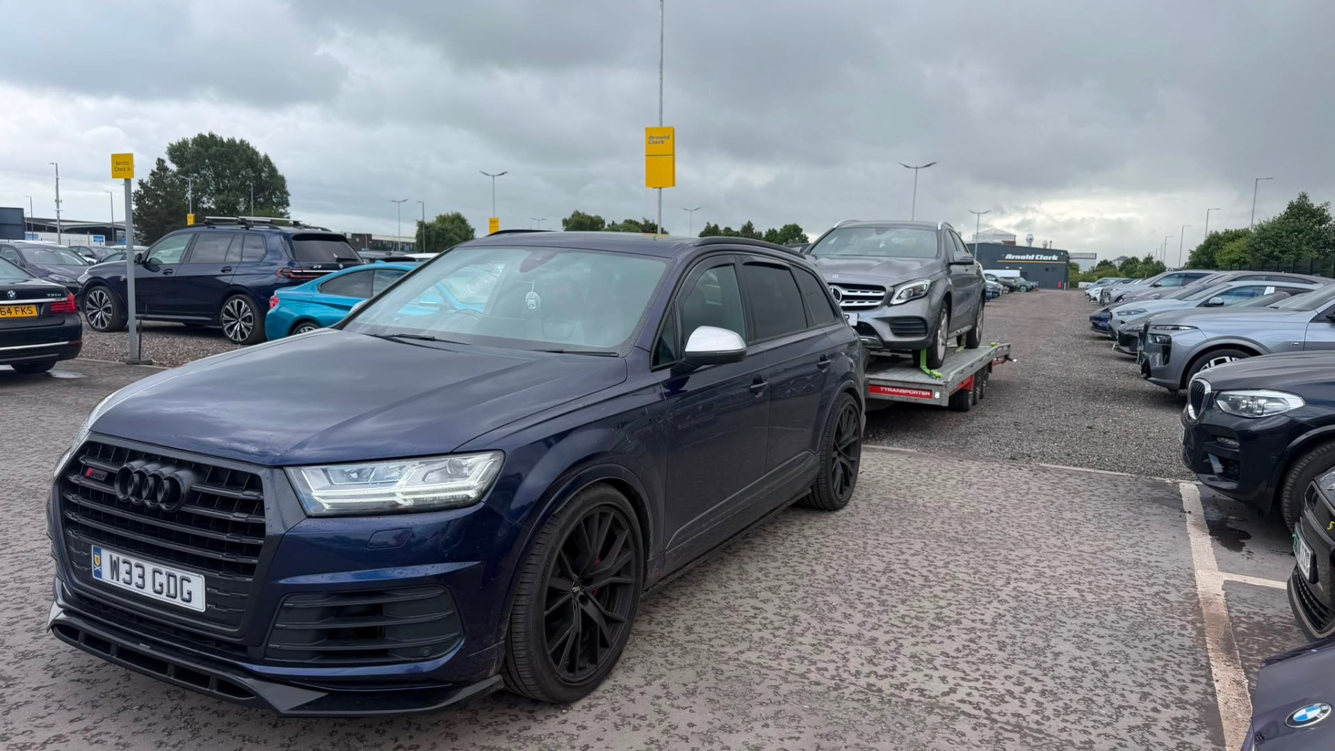 Blue Audi SQ7 towing Mercedes GLA on transporter at Arnold Clark